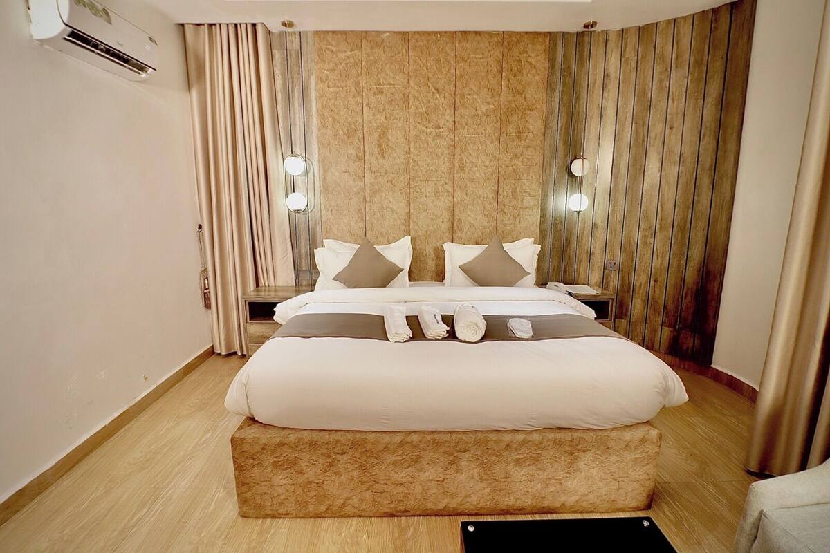 Une chambre d’hôtel moderne dotée d’un grand lit, d’un plancher en bois, d’un mur décoratif en marbre et d’un système de climatisation intégré.