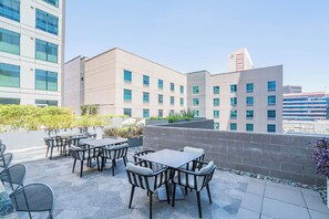 Eine Außenpatio mit Tischen und Stühlen, eine Steinmauer und der Blick auf ein modernes Gebäude mit vielen Fenstern.