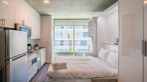 A modern hotel room with a bed, a small kitchenette, and a large window offering a city view. - Kenect 1310 (Phoenix)