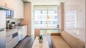 A modern kitchen with white cabinets, a built-in oven, and a coffee maker. There is a window with a view of buildings outside. - Kenect 1310 (Phoenix)