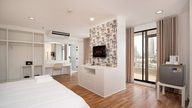 Una camera d'hotel moderna con un letto grande, una scrivania, un angolo trucco, una TV e un balcone con vista sulla città.
