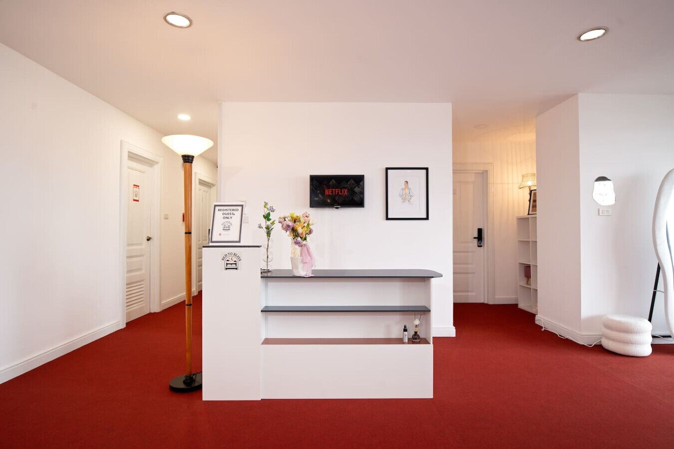 Un espace d’accueil avec un comptoir de réception blanc, des œuvres d’art encadrées et un sol recouvert d’un tapis rouge.