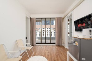 A modern hotel room with a large sliding glass door leading to a balcony, a flat-screen TV mounted on the wall, and a small kitchenette area. - Elegant King BR Apt& Bathtub, BTS Central BKK BTB8 (Pathum Wan)
