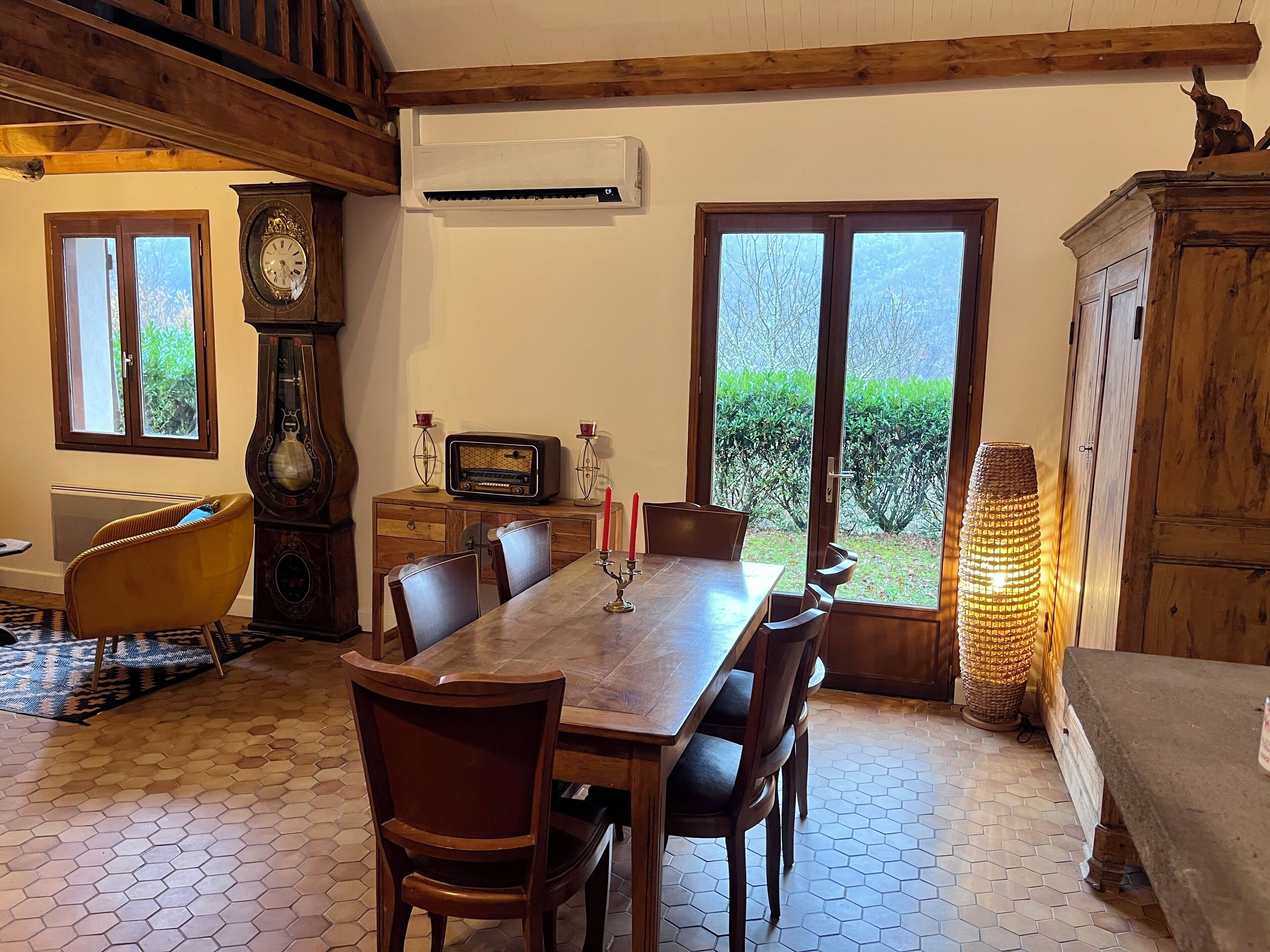 A dining area with a wooden table and chairs, a vintage radio, and a large window with a view of greenery.