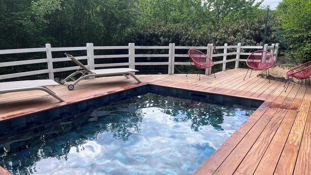 A wooden deck with a swimming pool, white fence, and red chairs.