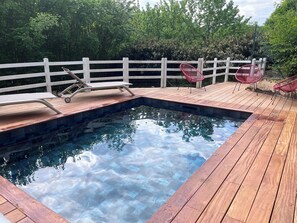 Une terrasse en bois avec une piscine, une clôture blanche et des chaises rouges.