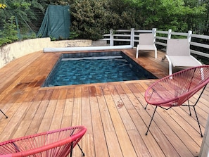 Una terraza de madera con una piscina pequeña, dos sillas de mimbre y una valla blanca.
