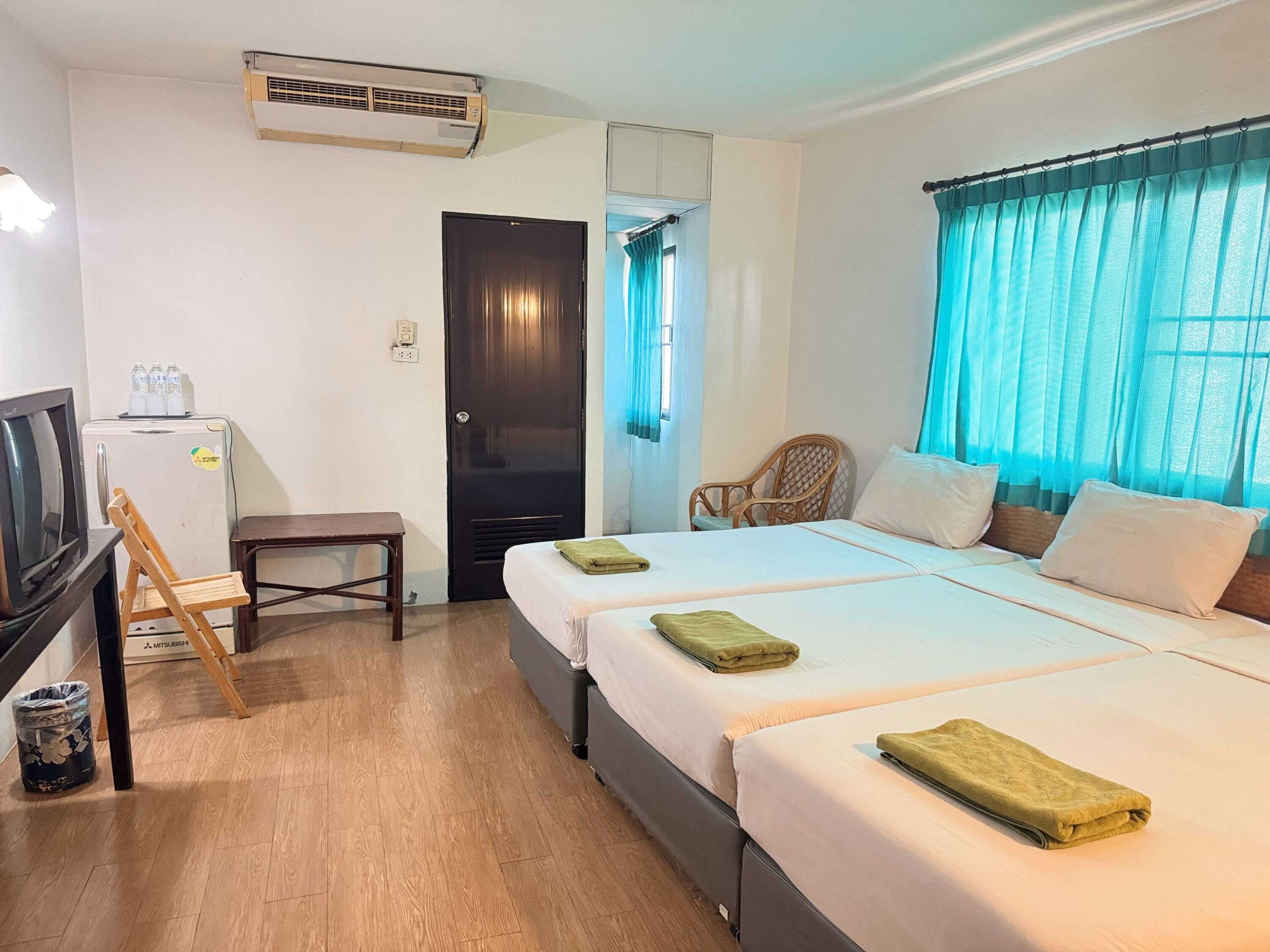 Una habitación de hotel con dos camas, televisión, refrigerador, una silla y ventana con cortinas.