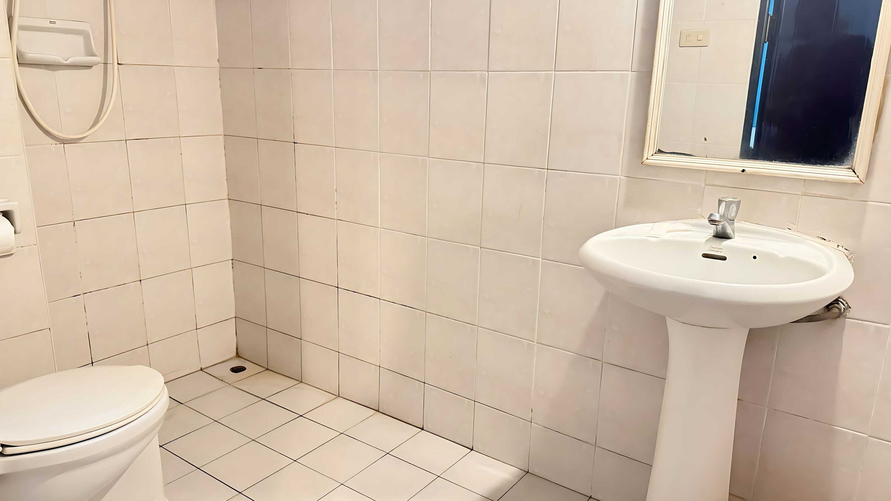 A bathroom with white tiles, a toilet, a sink, and a mirror.
