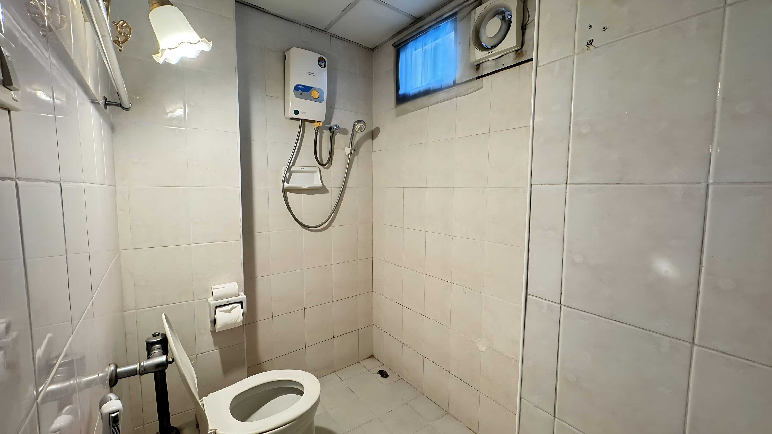 Une petite salle de bain carrelée, équipée de toilettes, d’un sèche-mains et d’un radiateur fixé au mur.