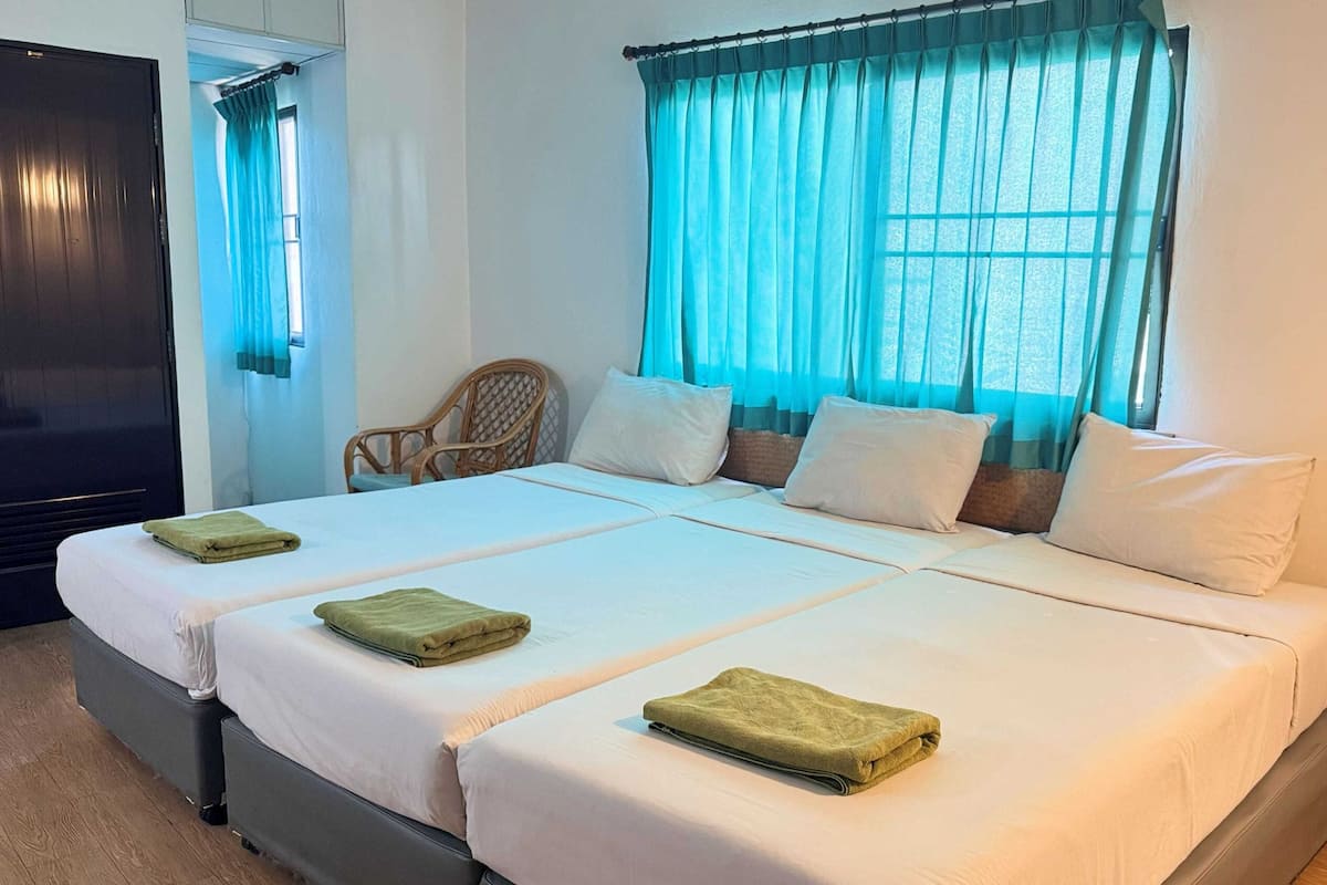 Habitación de hotel con cama doble, dos almohadas, una silla y ventana con cortinas.