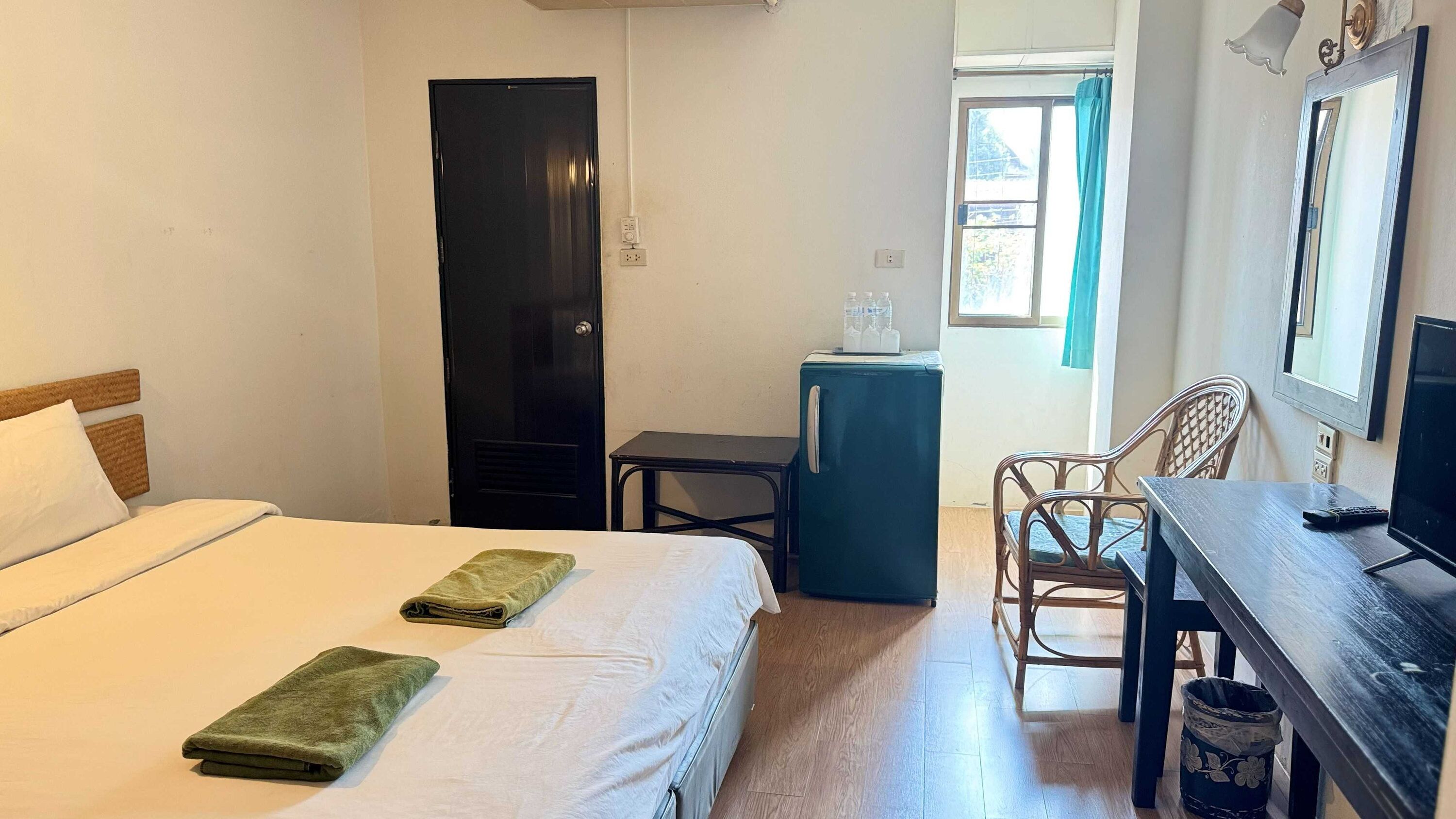 Habitación de hotel con cama, escritorio, silla, mesita, refrigerador y ventana con cortinas.