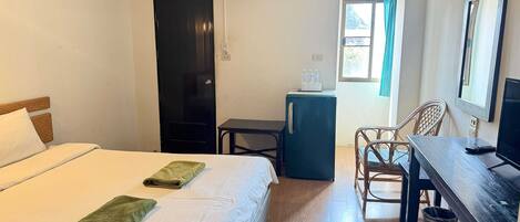 Habitación de hotel con cama, escritorio, silla, mesita, refrigerador y ventana con cortinas.