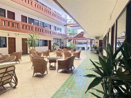 Un patio de hotel con mobiliario de mimbre, plantas en macetas y suelo de baldosas.