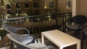 Varanda com cadeiras de vime e uma mesa, com vista para um edifício com várias janelas e varandas.