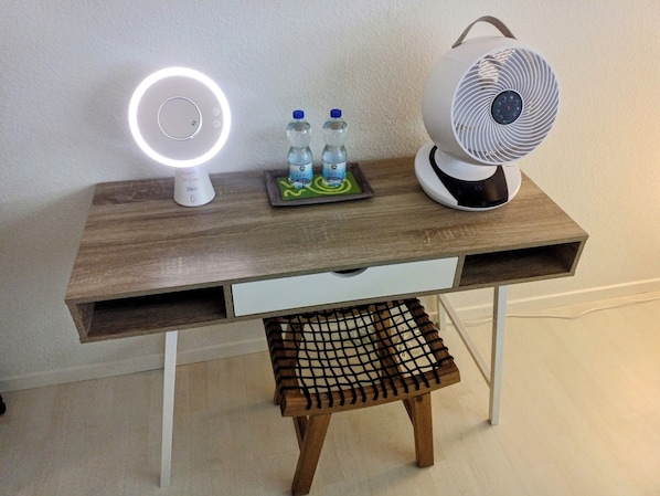 A wooden desk with a white lamp, two water bottles, a small tray with a green coaster, and a white fan. - Lucerne Center 4 (Luzern)