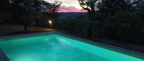 A swimming pool at dusk with a street lamp nearby.