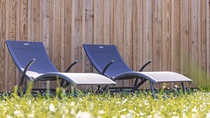 Dos sillones de descanso con estructura metálica y cojines, ubicados frente a una valla de madera.
