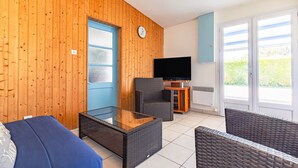 Una sala de estar con televisor, muebles de mimbre, una mesa de centro de vidrio y una puerta azul.