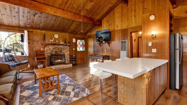 A cozy cabin interior with a stone fireplace, wooden ceiling, and a large bar area. - Bernhardt Brown Bungalow #2583 (Big Bear City)