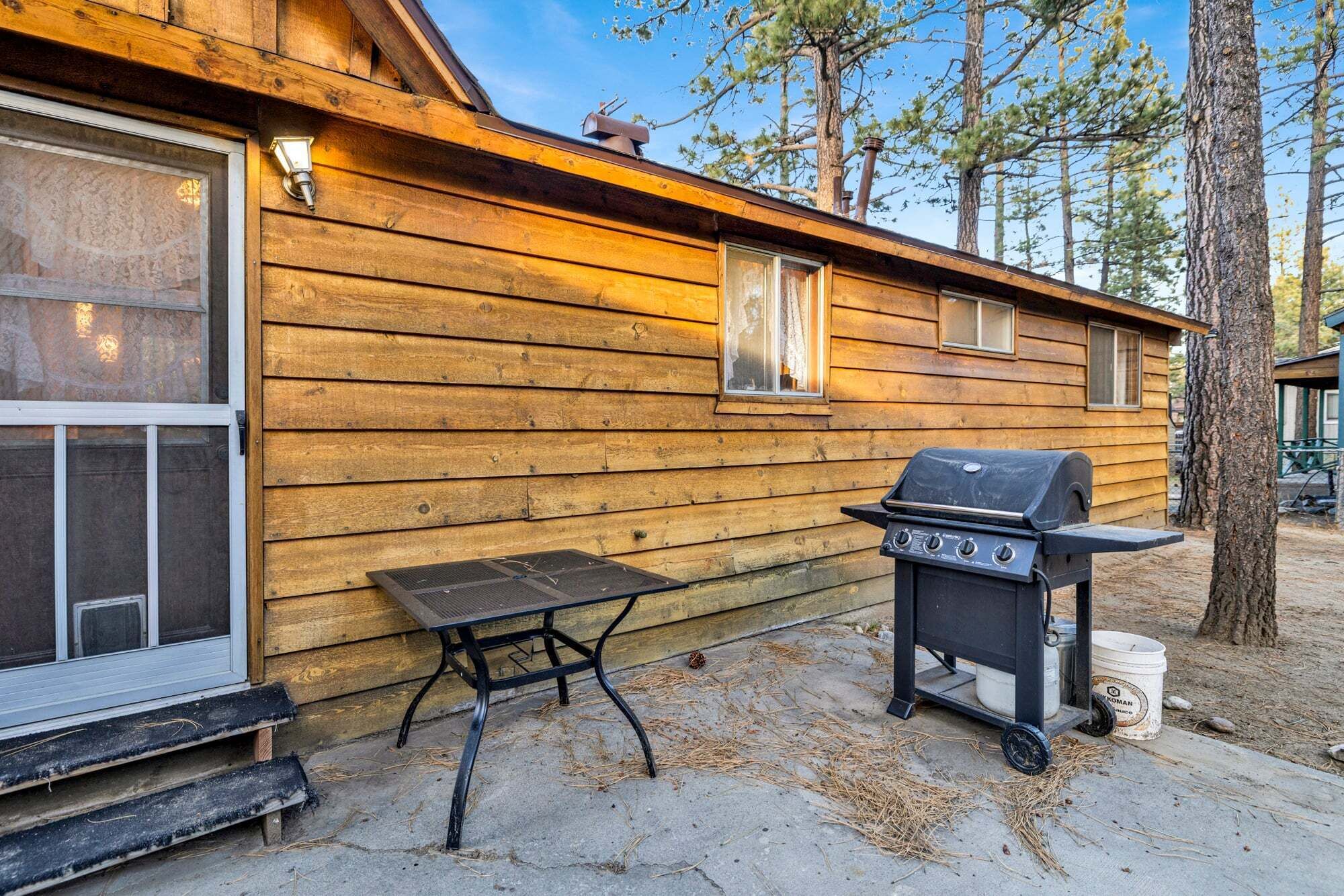 A wooden cabin with a grill and a table outside.
