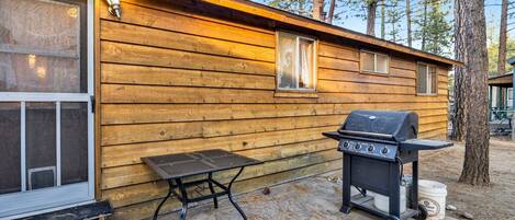 A wooden cabin with a grill and a table outside.