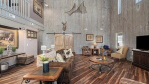 Une pièce spacieuse avec un plancher en bois, un grand mur en bois orné de têtes d’animaux empaillées, un canapé, une table basse et un téléviseur.