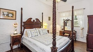 Una cama con dosel y tablero de madera, una mesita de noche con lámpara, un aparador y un espejo.