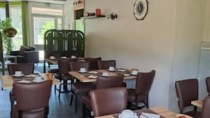 A restaurant with multiple tables and chairs, a clock on the wall, and a view of the outdoors. - hôtel le grand chêne (Gièvres)