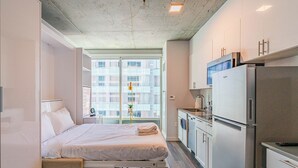 Een moderne hotelkamer met een bed, kitchenette en grote ramen met uitzicht over de stad.