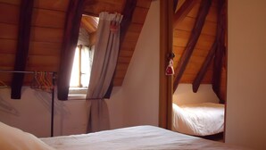 Ein Schlafzimmer mit schräg versiegelter Decke, einem Bett, einem Fenster mit Vorhängen und einer Hängeleuchte.