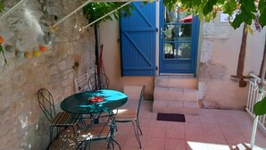 Eine Terrasse mit Tisch und Stühlen, eine blaue Tür und eine Steinmauer.