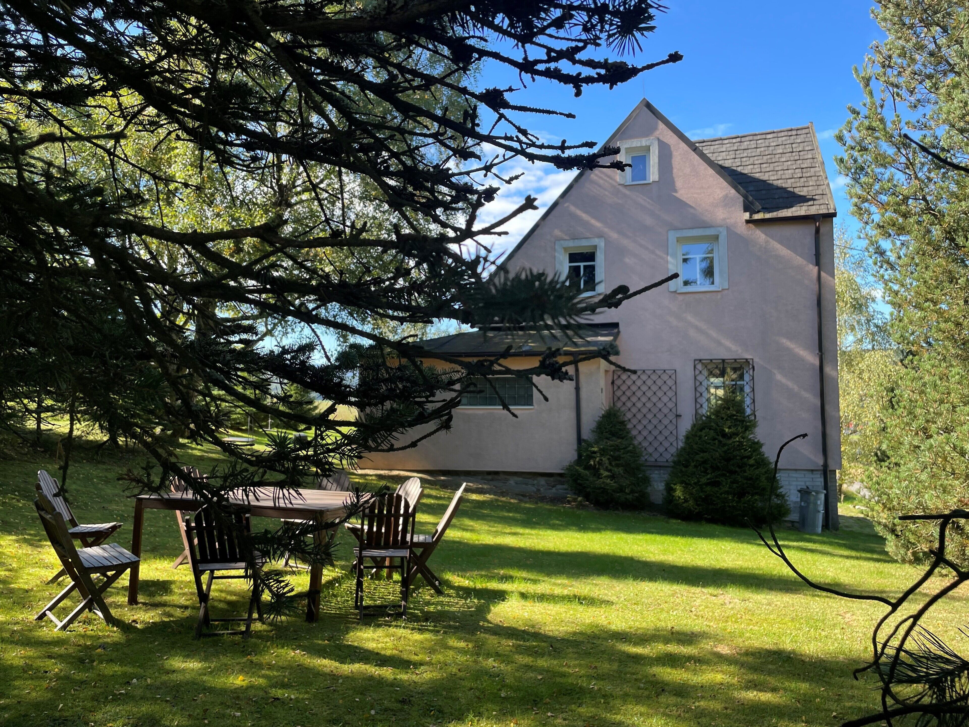 A house with a sloped roof, a fenced yard, and a patio with chairs and a table.