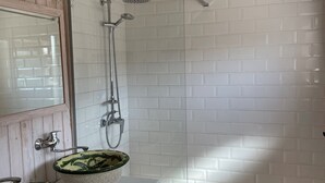 Een badkamer met houten plafond, witte betegelde wanden en een douchehoek.