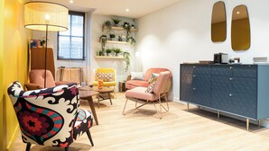 A modern living room with a sofa, chairs, a coffee table, a cabinet, and a window with plants on shelves. - 5 chambres en ville (Clermont-Ferrand)