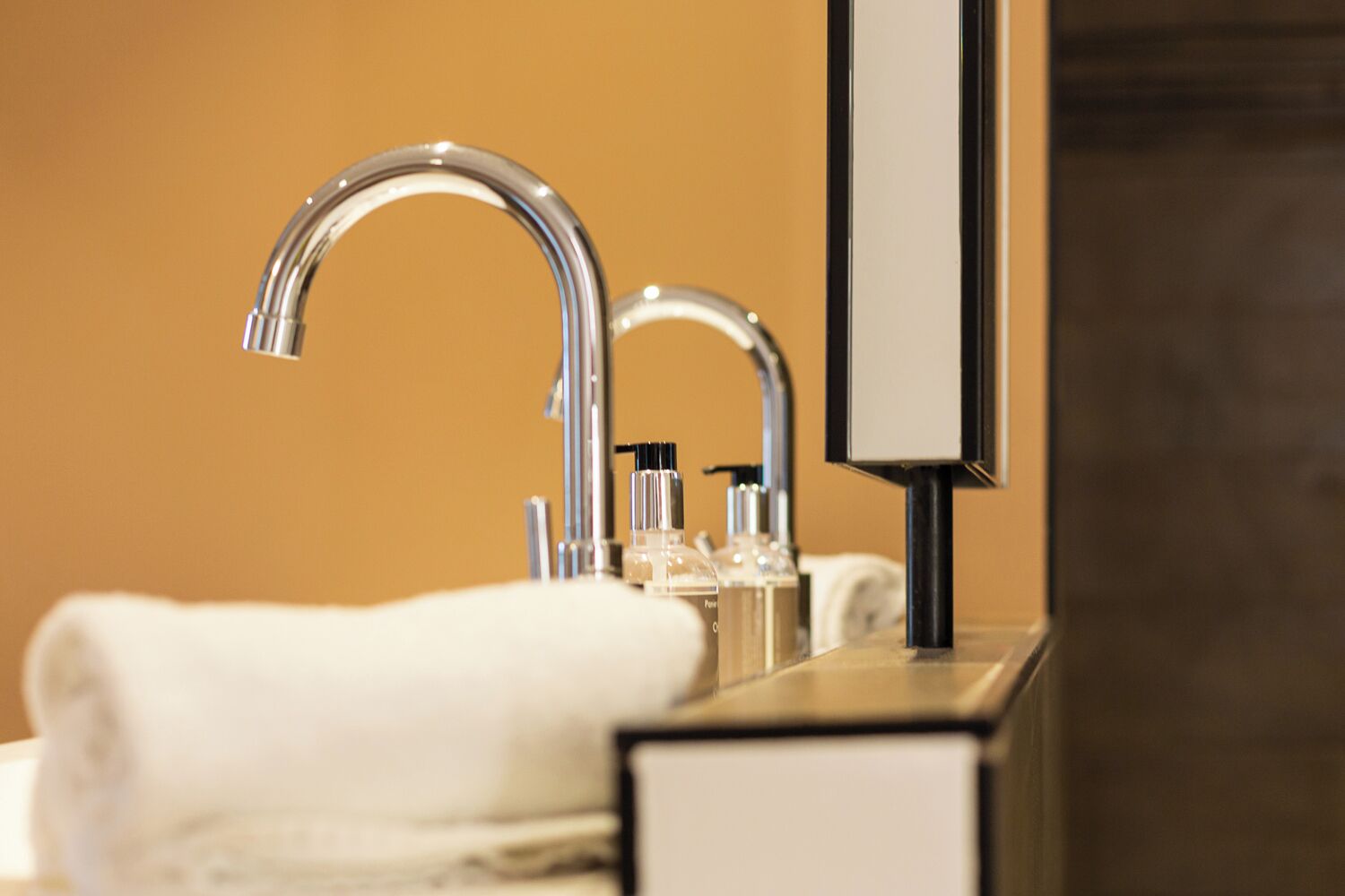 Une salle de bain moderne avec un robinet chromé, un miroir et des articles de toilette posés sur le comptoir.