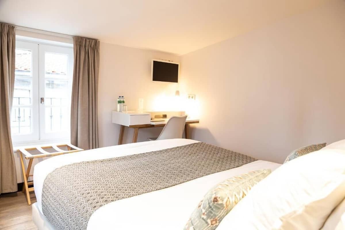 Een hotelkamer met een bed, bureau, stoel en een televisie aan de muur.