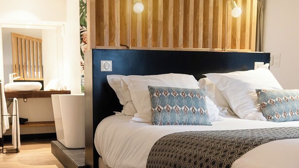 A modern hotel room with a large bed, a wooden headboard, and a bedside table with a lamp. - 5 chambres en ville (Clermont-Ferrand)