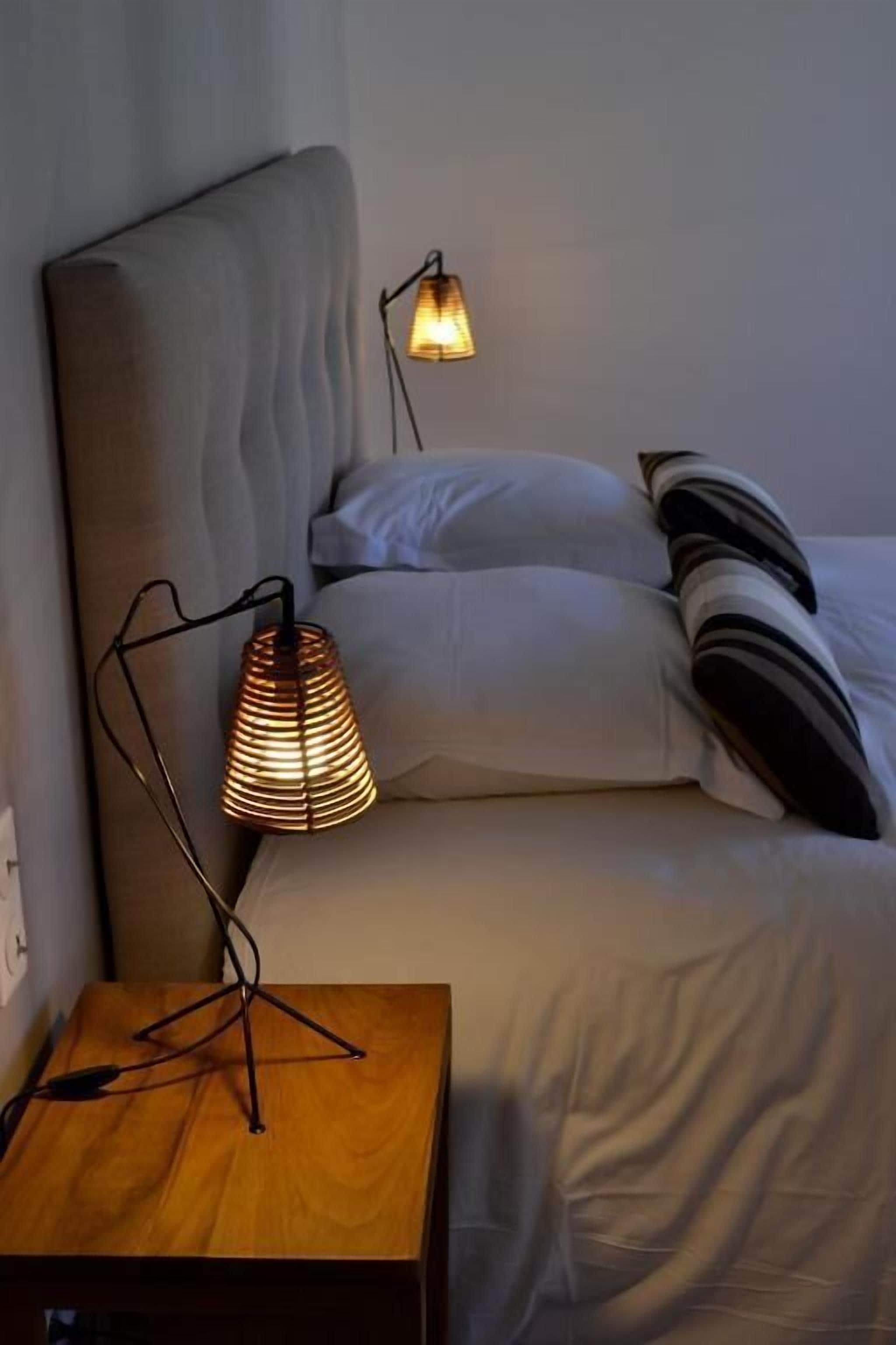 A bedroom with a bed, a bedside table with a lamp, and a wall-mounted lamp.