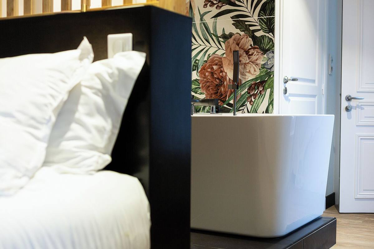 Een bed met witte lakens, een zwart hoofdbord en behang met een bloemmotief.