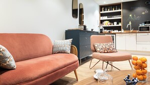 A modern living room with a sofa, armchair, and coffee table. There is a kitchen area with cabinets and a microwave. - 5 chambres en ville (Clermont-Ferrand)
