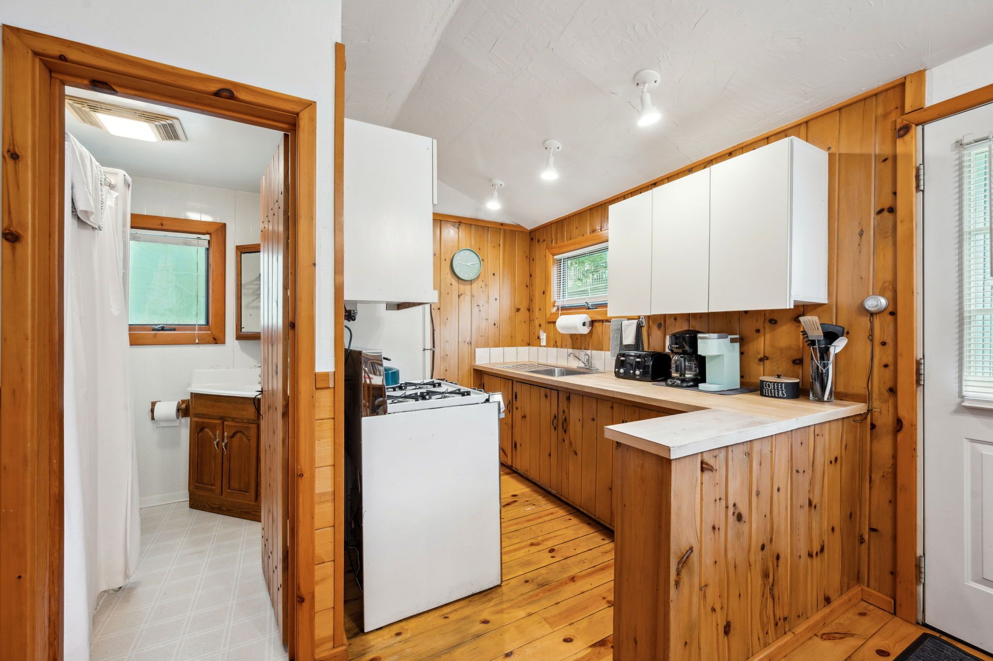 Una cocina compacta con paneles de madera, una estufa a gas, una cafetera y un lavabo.