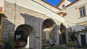 Un patio con arcos de piedra, un carro de madera y un jardín con plantas en macetas.