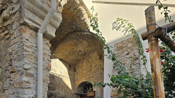 Un estrecho pasillo de piedra con una puerta de madera, paredes de piedra y un poste de madera con una cuerda.