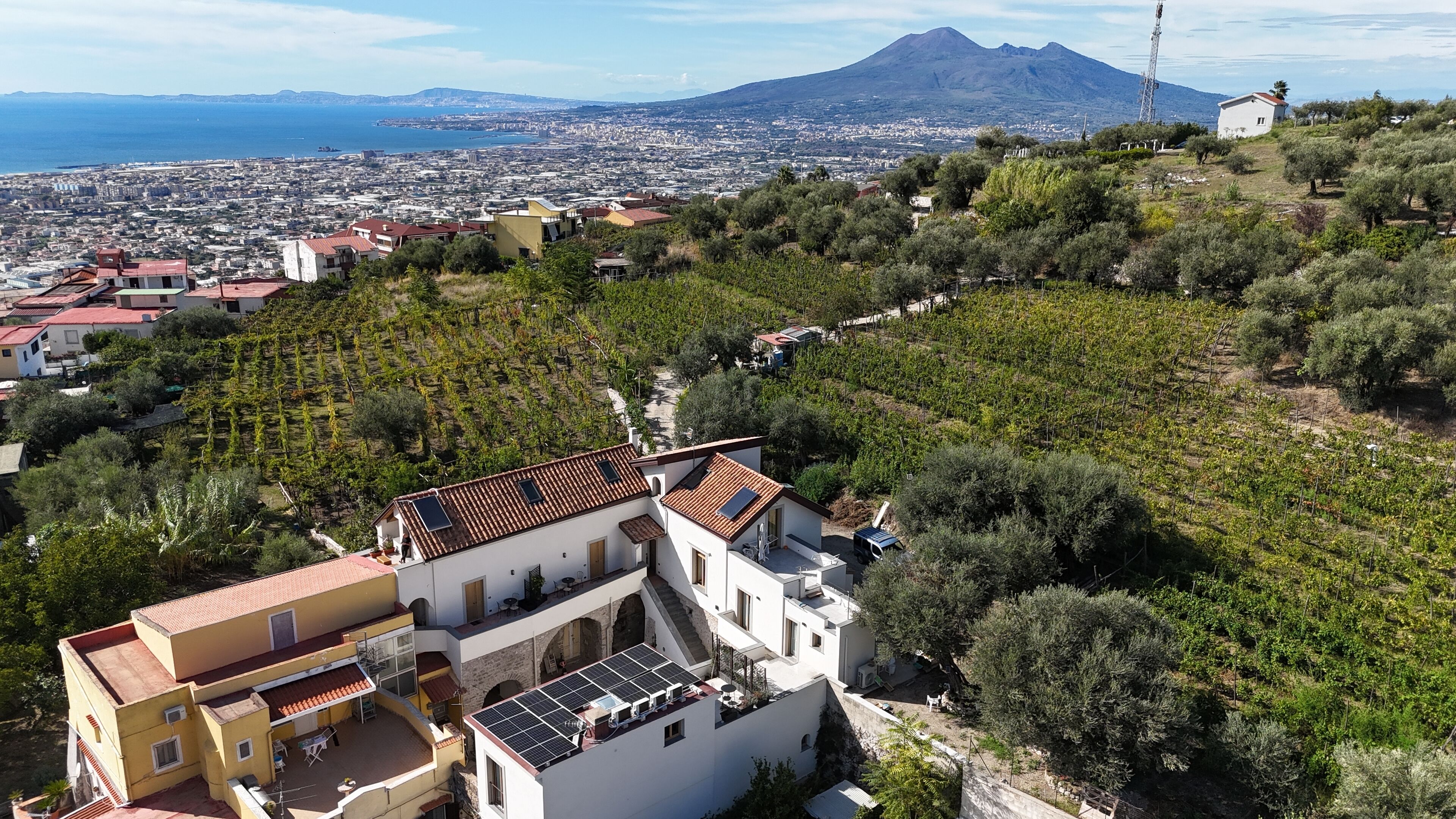 A residential building with a sloped roof, solar panels, and a view of a cityscape and a mountain in the distance.