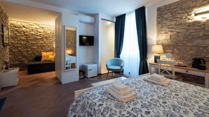 Habitación de hotel con pared de piedra, cama con colcha estampada, escritorio con lámpara, una silla y televisor montado en la pared.