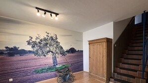 Una stanza con un murale raffigurante un albero e un campo, pavimento in legno, un armadietto in legno e una scala.
