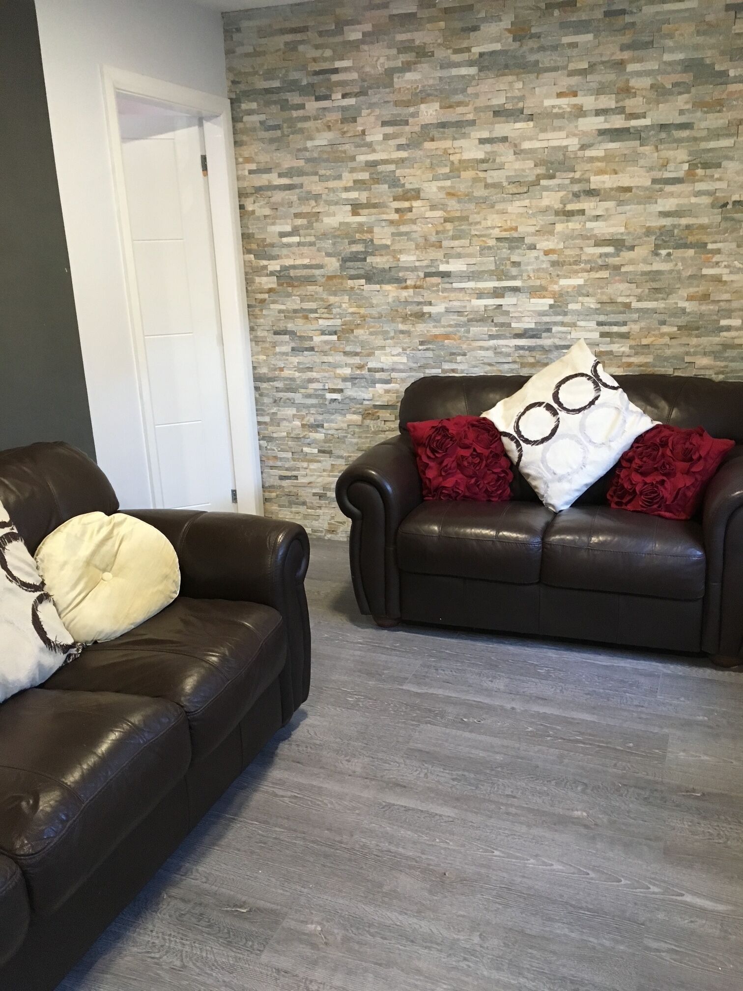 Dos sofás de cuero con cojines, una pared con diseño de piedra y suelo de madera.