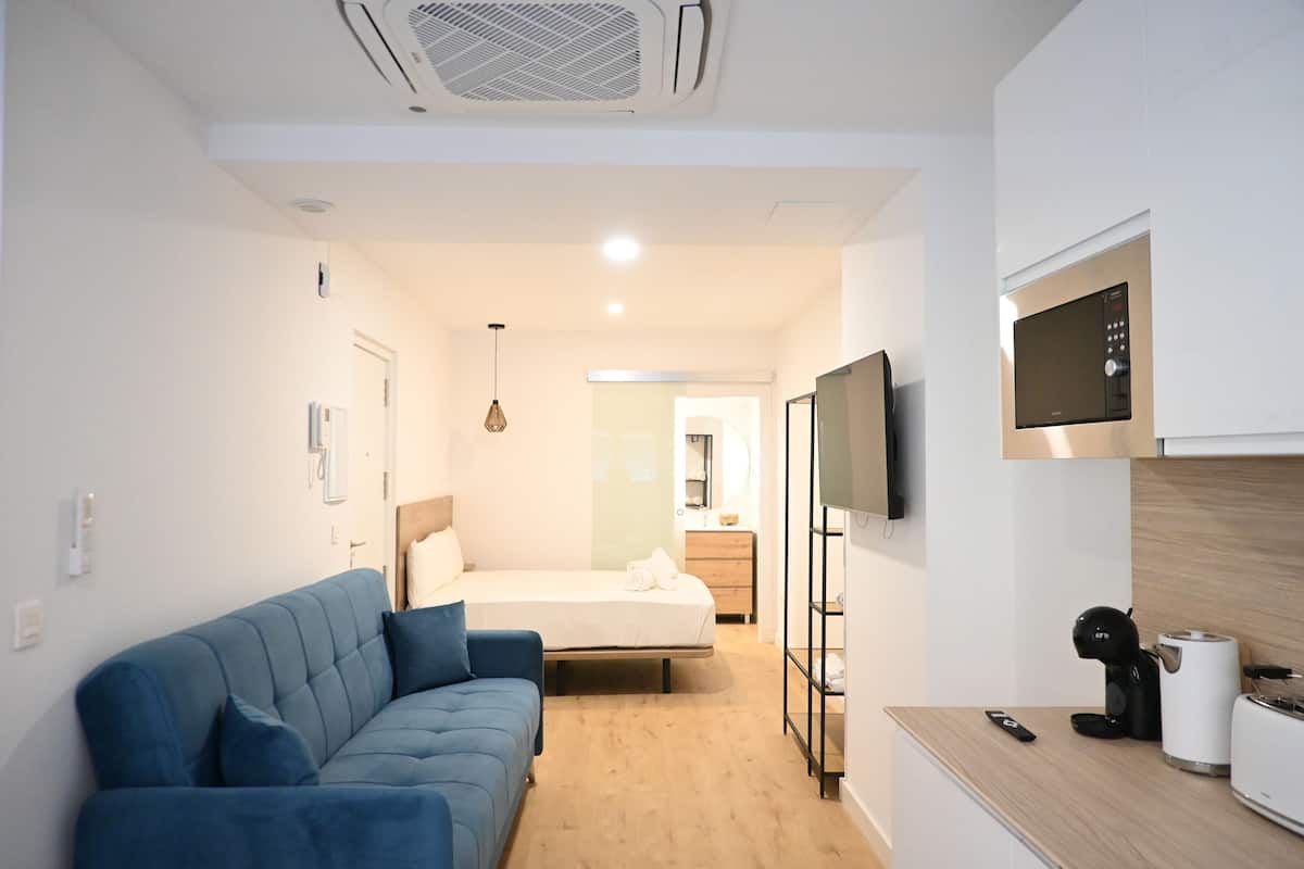 Una habitación de hotel moderna con sofá, cama, televisor montado en la pared, cafetera y mostrador de madera.