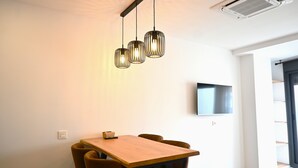 Een moderne eetruimte met een houten tafel en bruine stoelen, een plafondlamp en een wandgemonteerde flatscreen-televisie.